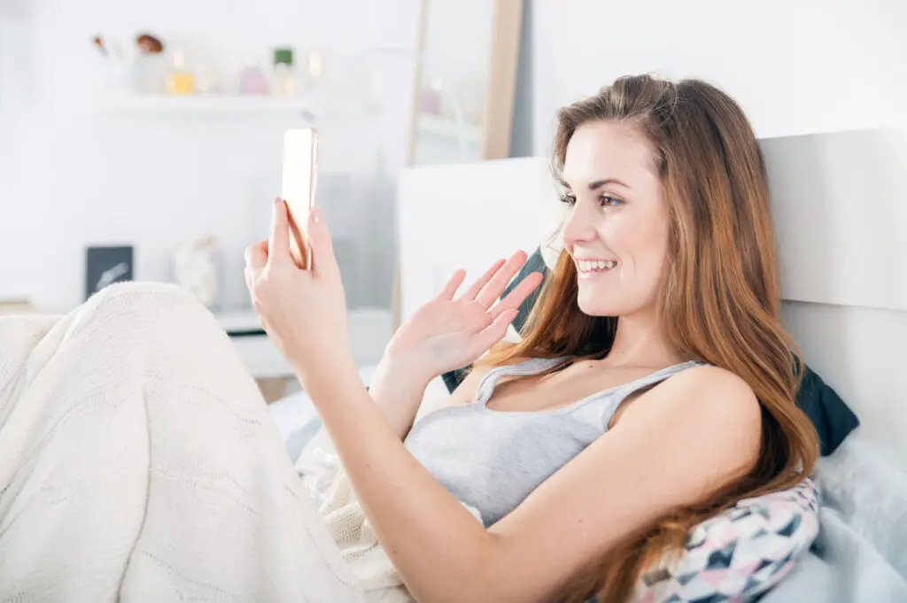 Young woman lying in bed and video calling on smart phone