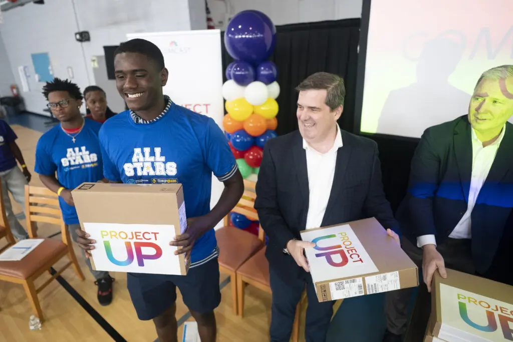 Student smiles after receiving a laptop from Mike McArdle and Mike Mitchell of Comcast, right, during the Greenwood Comcast Expansion Rally at the Boys & Girls Club Thursday May 22, 2025, in Greenwood, S.C.