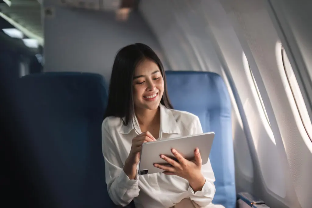 Passenger seated on plane using phone to shop holiday deals and Cyber Monday savings during travel.