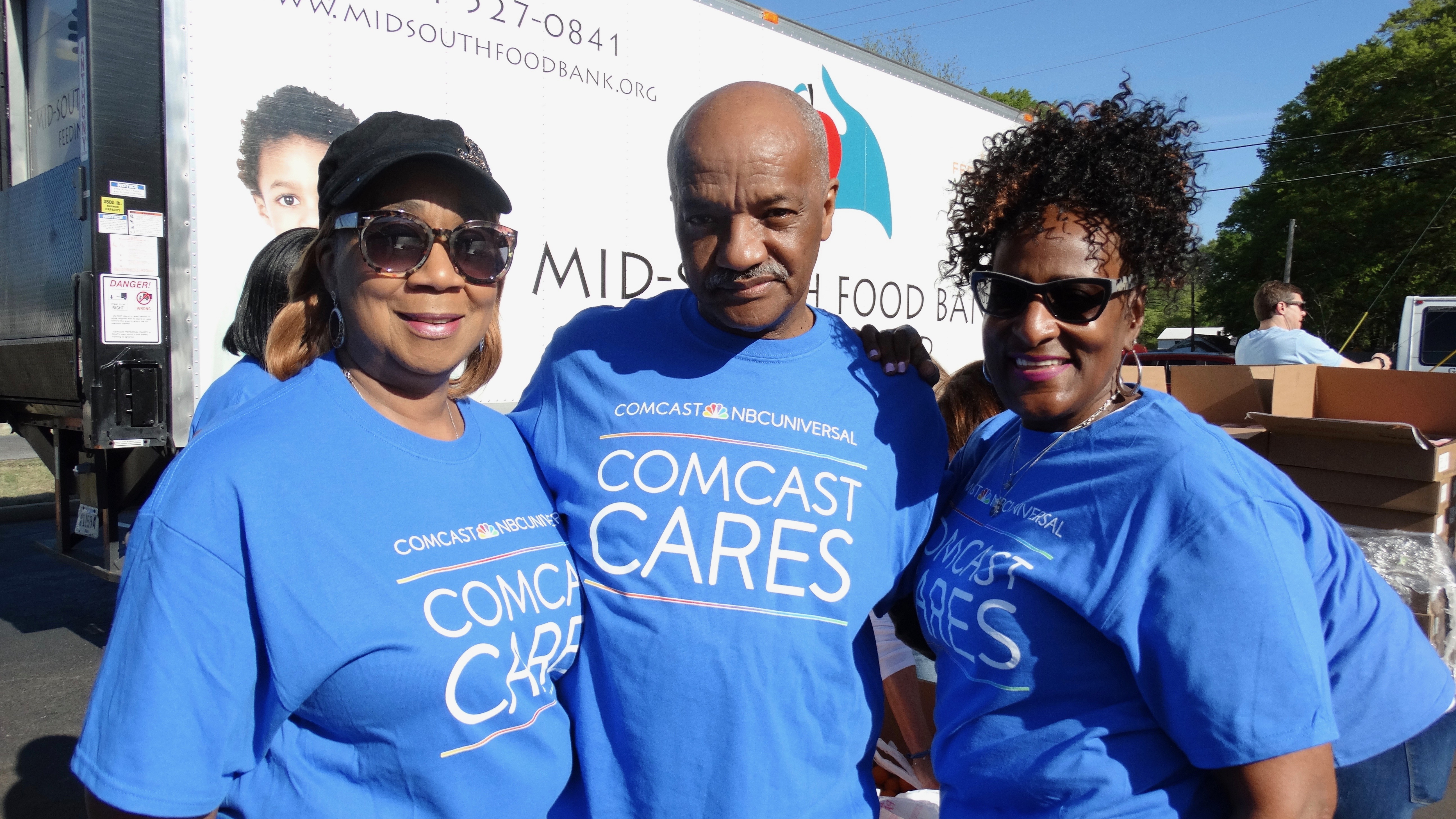 Three Comcast Cares Day volunteers stand in front of a food bank truck.