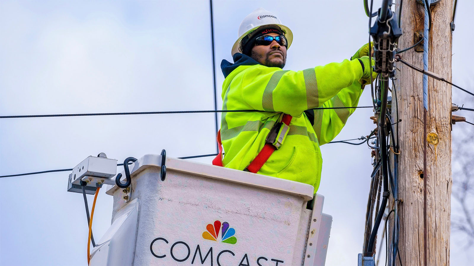 A Comcast technician repairs equipment on a telephone pole.