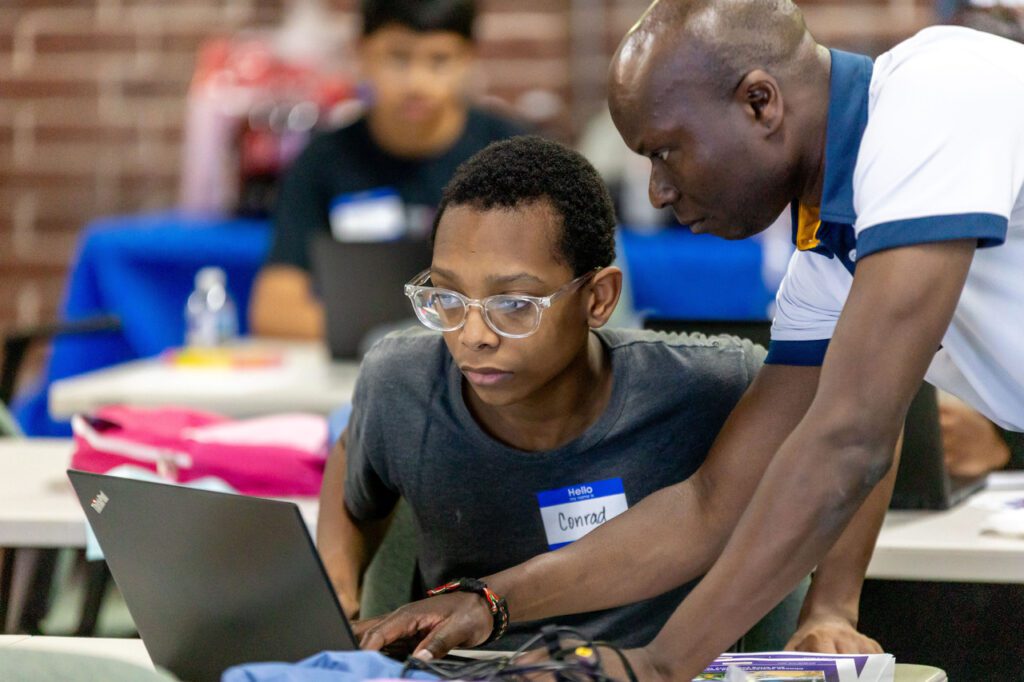 Man assists student who is working on a laptop