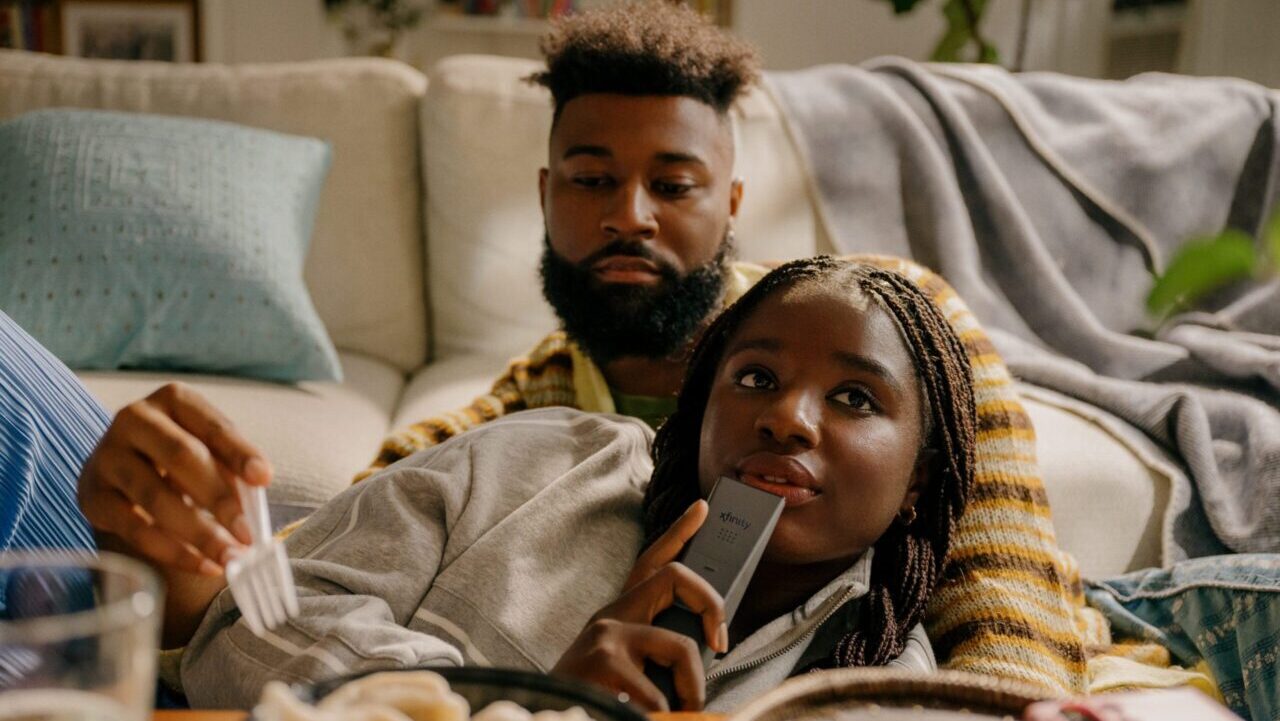 A man and woman relaxing on a sofa. The woman is using an Xfinity Voice Remote.