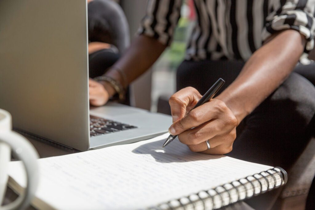 Man using a laptop, writing in a notebook