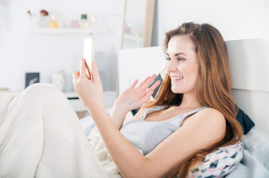 Young woman lying in bed and video calling on smart phone