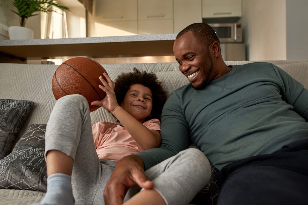 A father and son are watching basketball on a couch. March madness fans are not only watching multiple games with Xfinity Multiview but keeping up with their March Madness brackets and scores only with Xfinity.