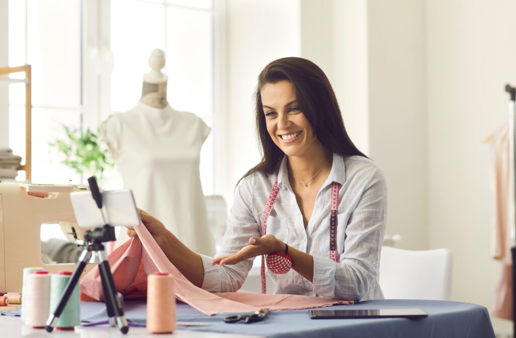Xfinity Mobile customer in the South enjoys fast WiFi on their device on the Premium Unlimited plan. IMAGE: Friendly seamstress conducts an online sewing masterclass while sitting in her own workshop. Woman records video lesson sitting in front of phone standing on tripod. Small business and hobby concept.