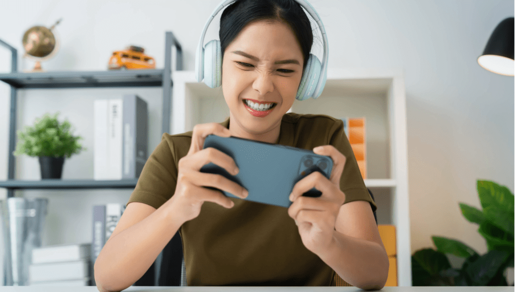 Xfinity Mobile customer in the South utilizing new Premium Unlimited plans 4K streaming and hotspot data on WiFi. IMAGE: Young female in a living room with headphones enjoys gaming on her cell phone.