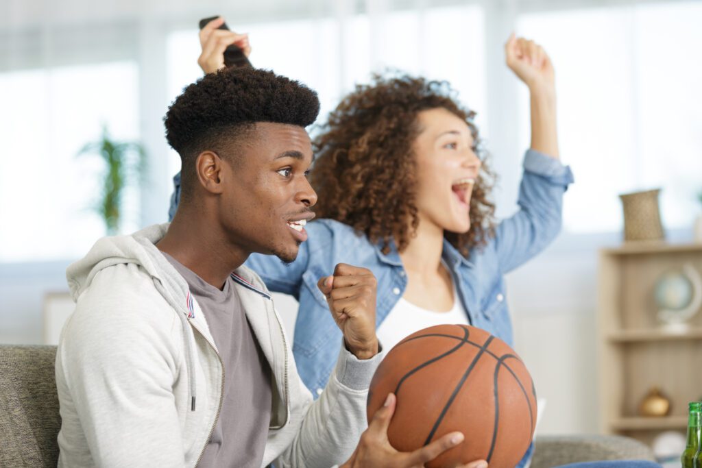 Watching NBA basketball at home with Xfinity, holding a basketball and enjoying the game.